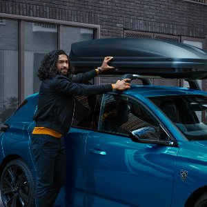 Man securing a roof box on a blue car with a Peugeot logo.