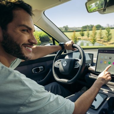 Man driving a car while using a touchscreen interface on the dashboard.
