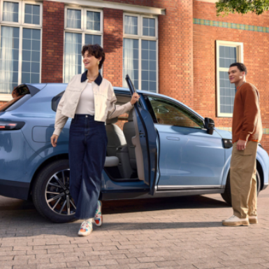 Two people near a blue SUV with its rear door open, in front of a building.