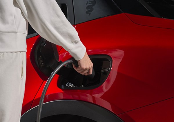 Person charging a red electric vehicle.