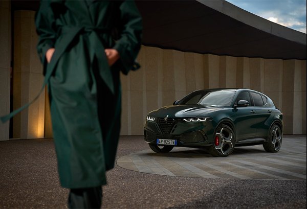 A person in a green coat walking past a parked dark green SUV.