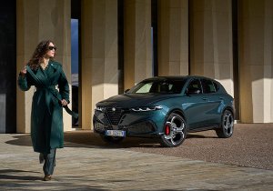 A person in a green coat walks near a green car parked in an urban setting.