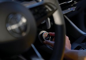 Hand adjusting a control knob inside a car, with part of a steering wheel visible.