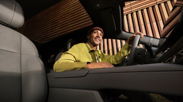 Man in a yellow shirt driving a car, viewed from the passenger side.