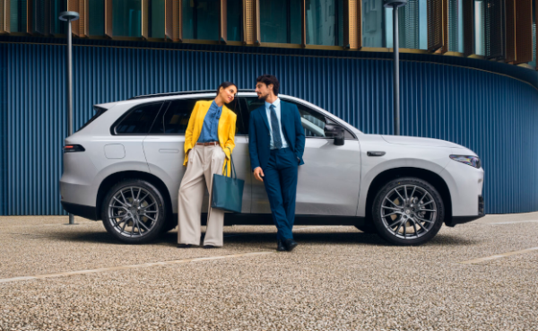 Two people in smart attire leaning on a white SUV parked outside a building.