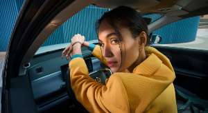 Person in a yellow coat seated in a car, looking back through an open car door.