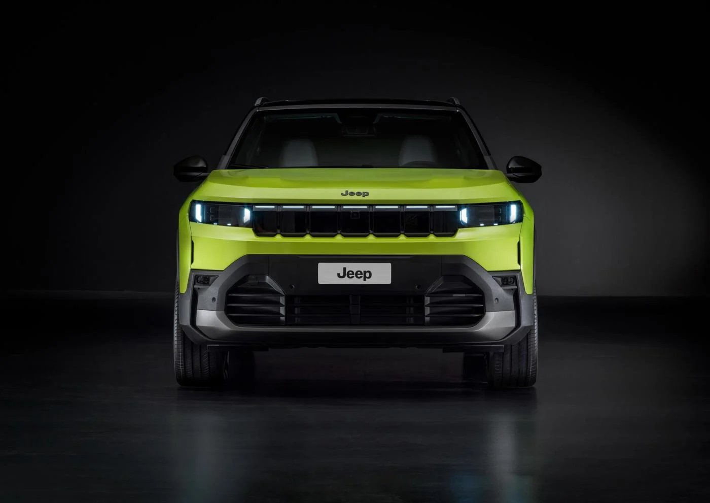 Front view of a green Jeep SUV with headlights on.
