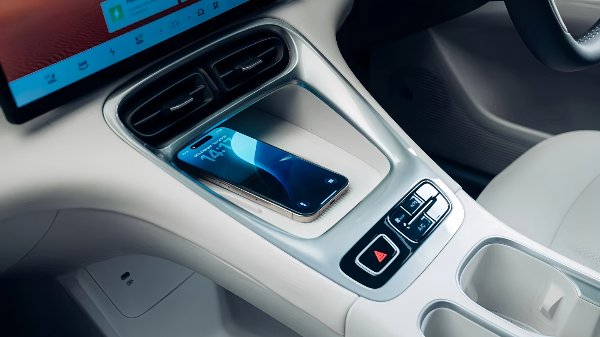 Smartphone charging wirelessly in a car's central console with a digital display above.