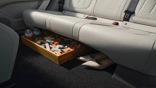 Children's toys and bottles in a box under a car seat beside beige pointed shoes.