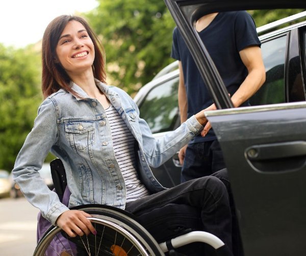 Woman in a wheelchair smiling while entering a car with assistance.
