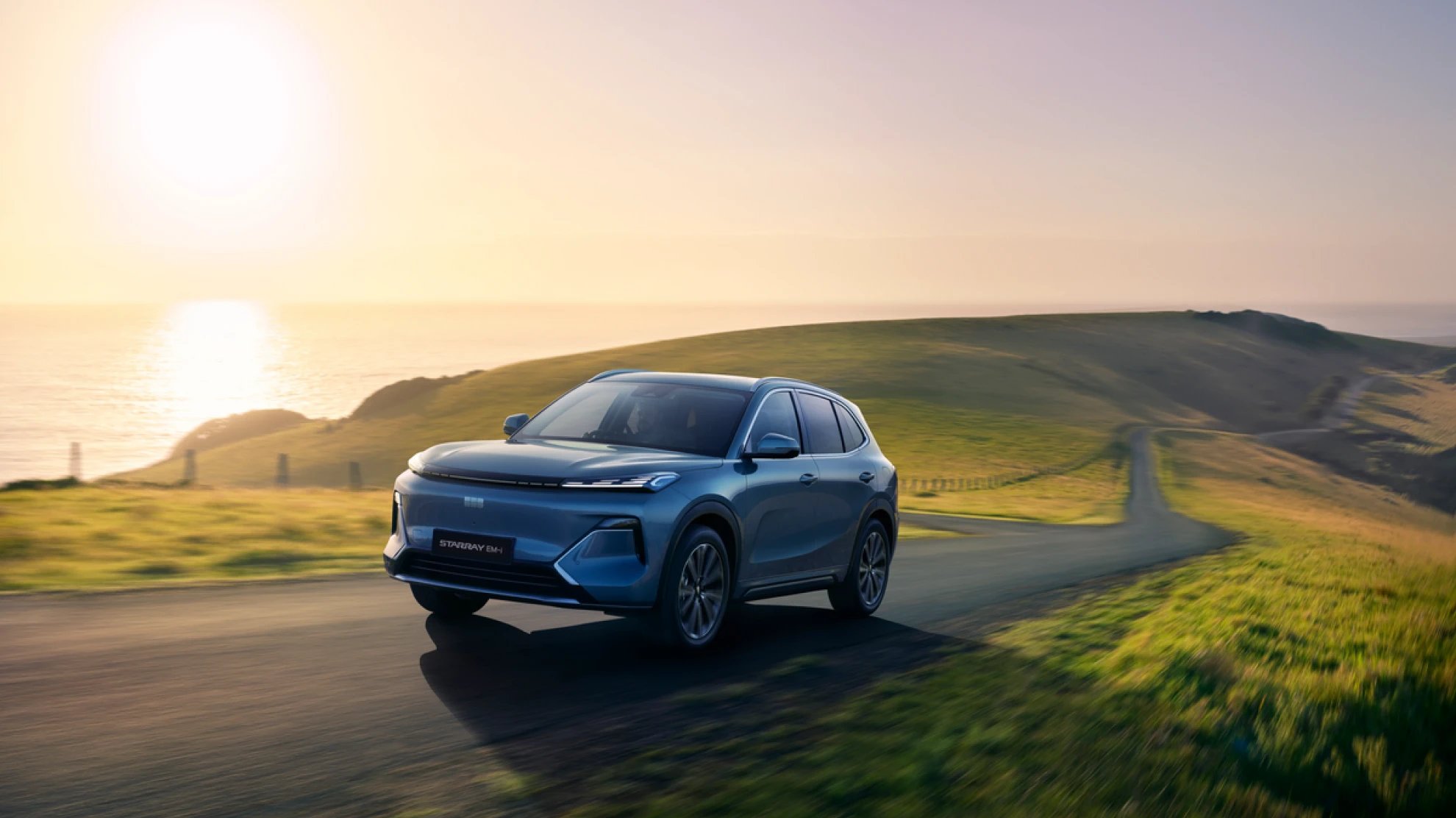 Blue SUV driving on a rural road during sunset.