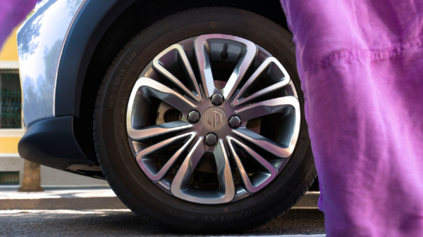 Close-up of a car wheel with a five-spoke alloy rim. Person in purple clothing slightly visible.
