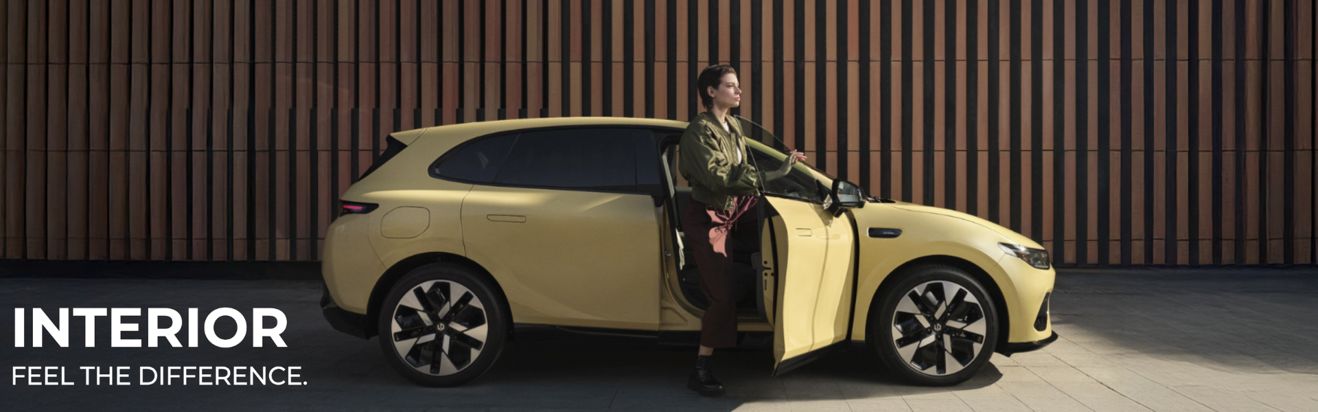 Person exiting a yellow car with front door open, wooden wall in the background.